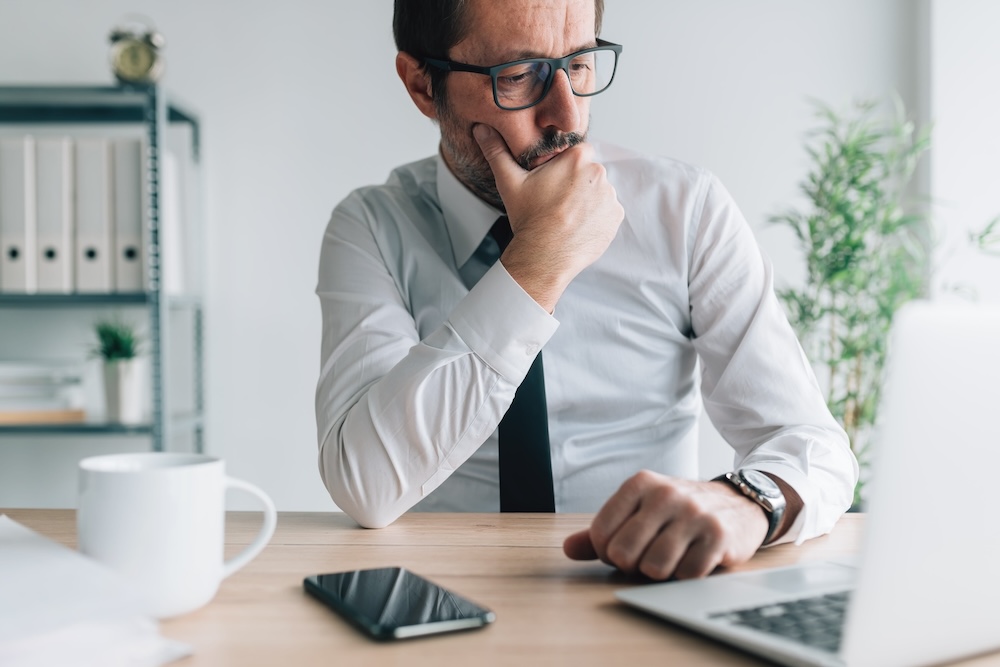 Businessman considering manufacturing energy savings while looking at a laptop.
