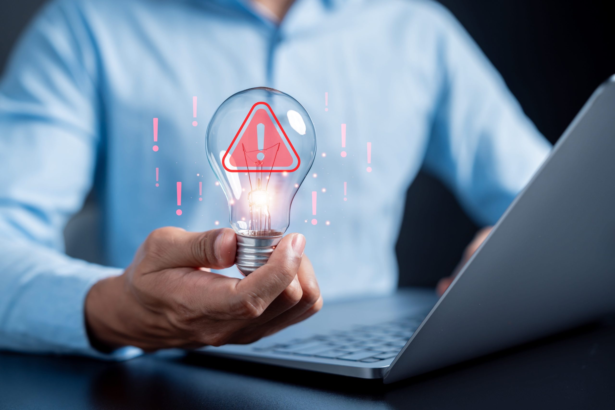 Man in blue shirt holds lightbulb graphic while looking at laptop considering MHHS changes